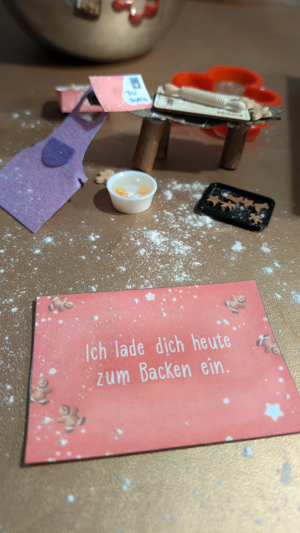Wichtelszene mit verstreutem Mehl und der Karte: Ich lade dich heute zum Backen ein