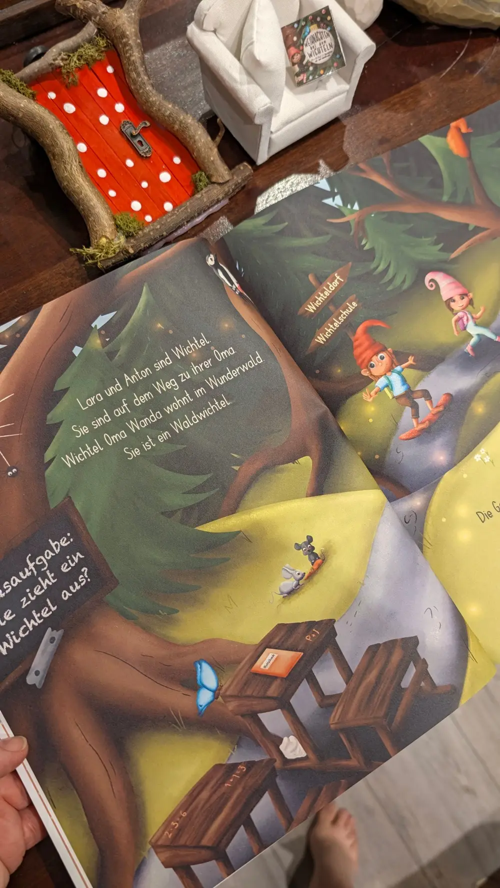 Aufgeschlagenes Buch Band 2: Lara und Anton auf dem Weg zur Wichtelschule, an der Tafel steht die Hausaufgabe Wie zieht ein Wichtel aus?
