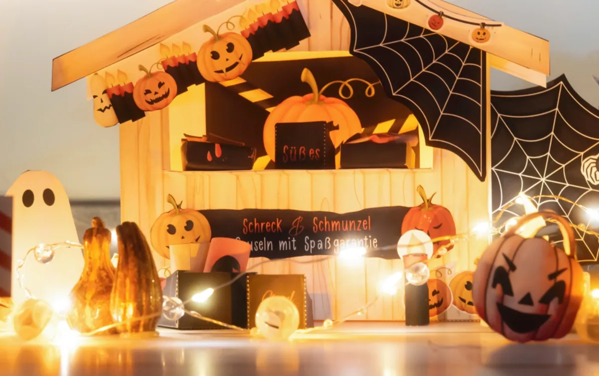 Halloween-Marktstand vor der Wichteltür mit Kürbissen, Spinnennetz, Fledermaus, Gespenst und Schild Schreck und Schmunzel