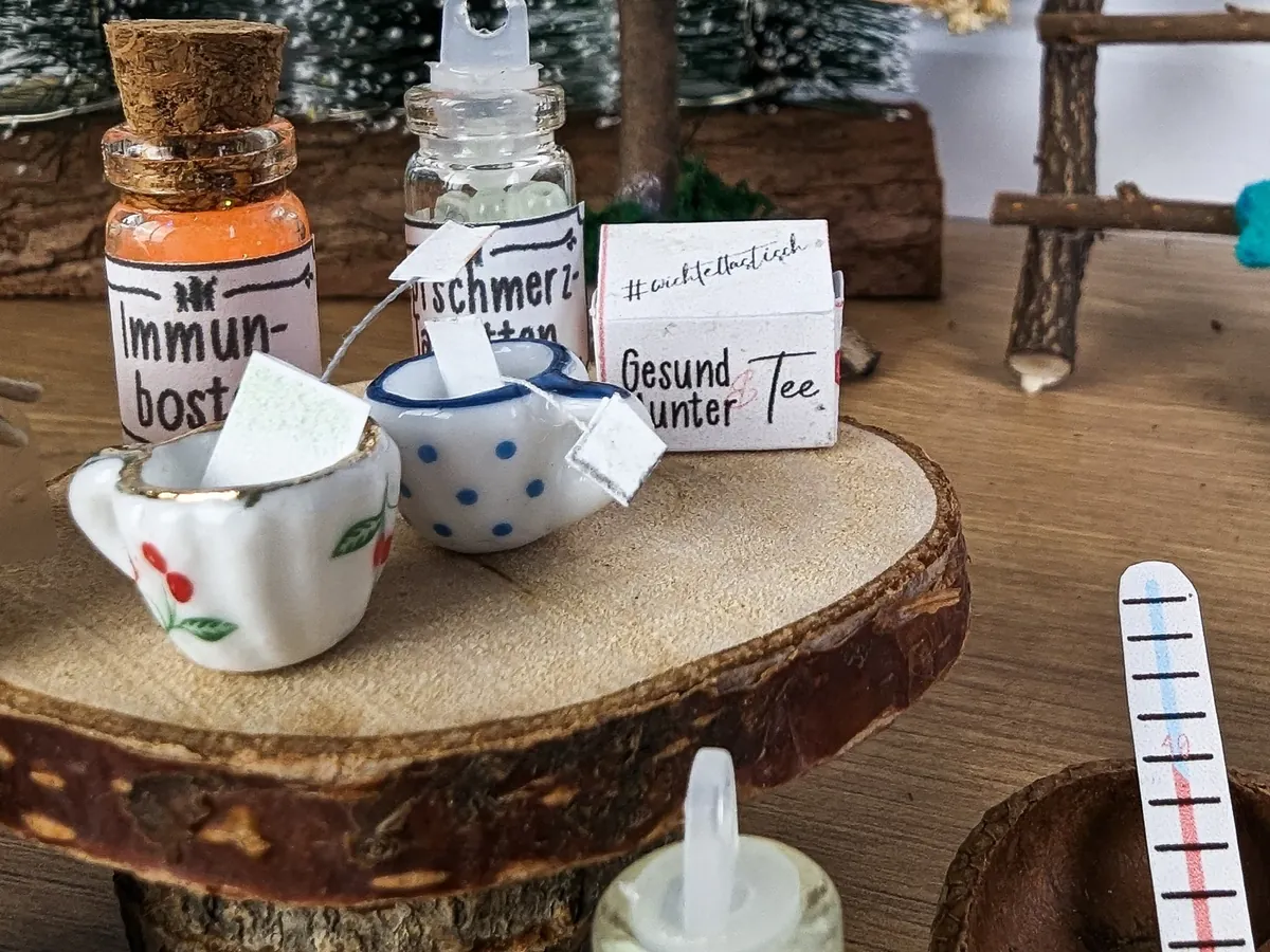 Mini-Teetassen mit Teebeutel, Fläschchen Immun-Boost und Packung Gesund-unter-Tee auf einer Baumscheibe
