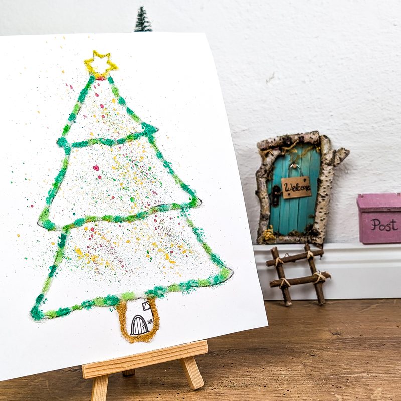 Bastelidee aus dem Starterpaket: gebasteltes Tannenbaum-Bild auf einer kleinen Staffelei neben der Wichteltür